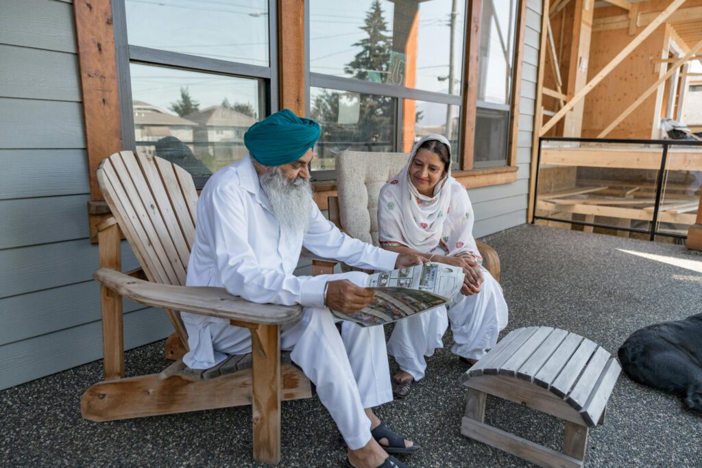 pexels-photo-14769678-14769678 A senior couple in traditional attire sits on a patio, reading a newspaper.